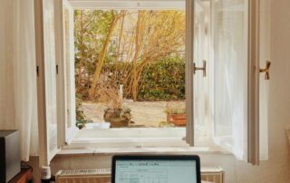 Laptop on a table in front of open windows overlooking a garden, representing flexible grant writing support.