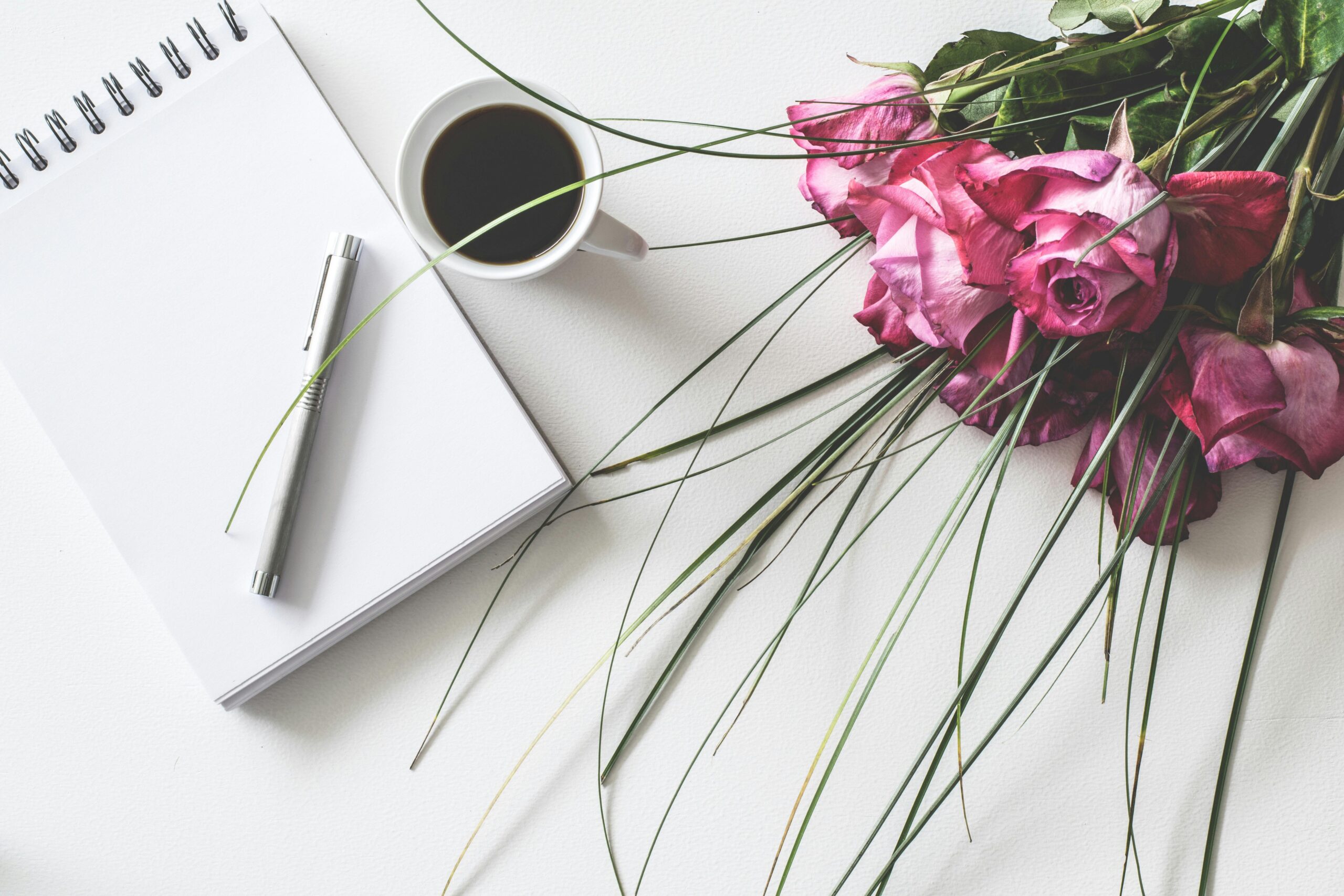 A bouquet of pink roses, a cup of coffee, and an empty notebook with a pen, symbolizing open conversation. 