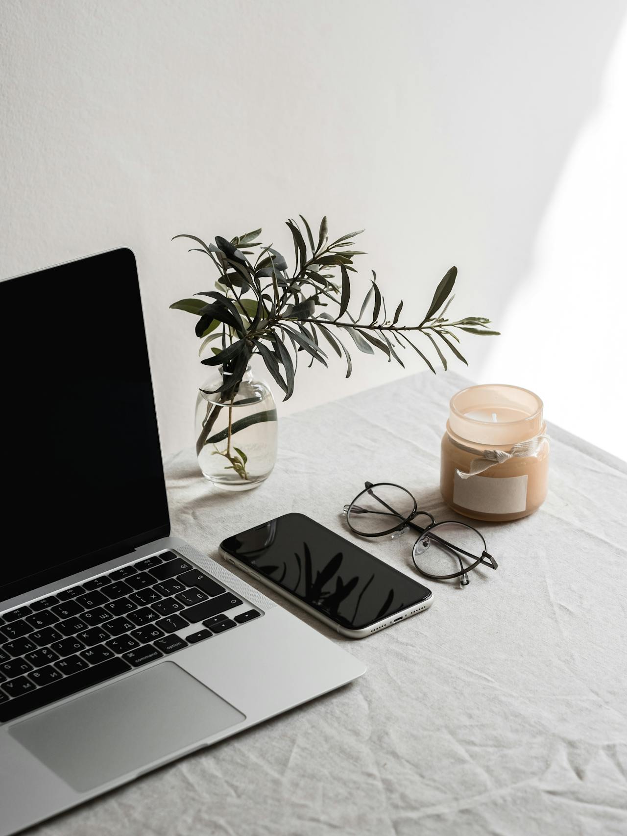 Laptop, smartphone, glasses, and candle on a desk with a vase of greenery – modern workspace for grant writing and storytelling at Pressed & Poured.